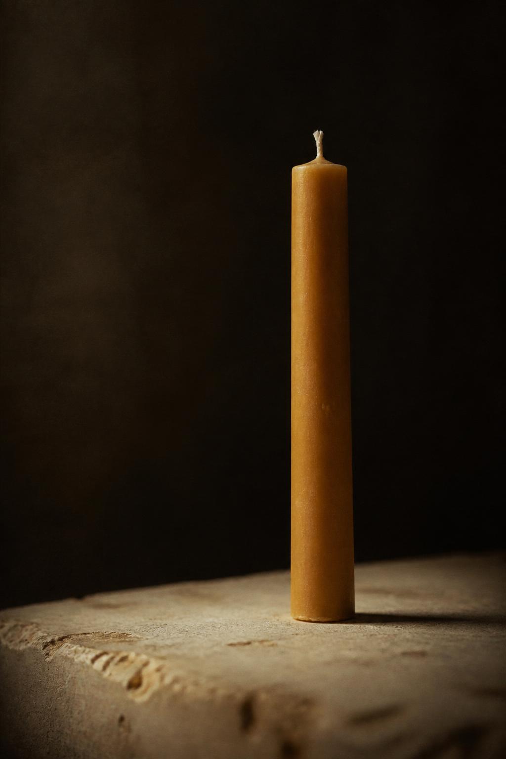 A single unlit beeswax taper candle on weathered stone.
